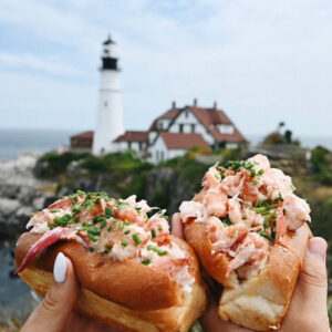 bite into maine lobster rolls with lighthouse in the background